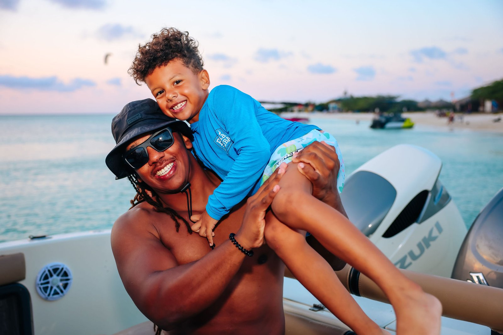 A man holds a smiling child aboard the Malmok Charters boat at sunset in Aruba