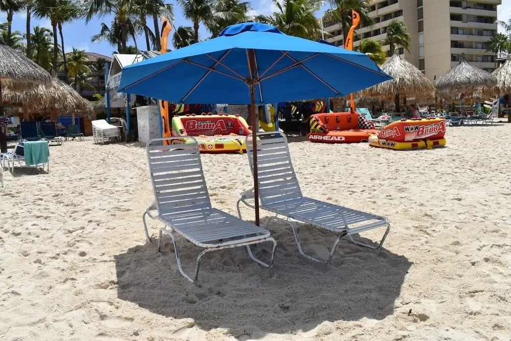 Beach umbrella and two chairs set up on the sand in Aruba, ready for guests