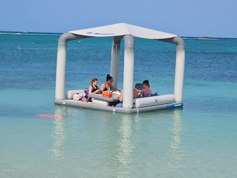 Two guests lounging on cushions under a floating lounge canopy in calm shallow water