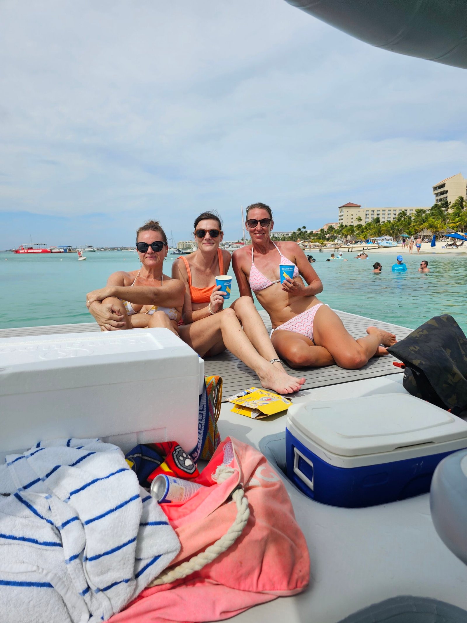 Three friends relaxing on an Aruba Aqua Lounge with the coolers and drinks they brought