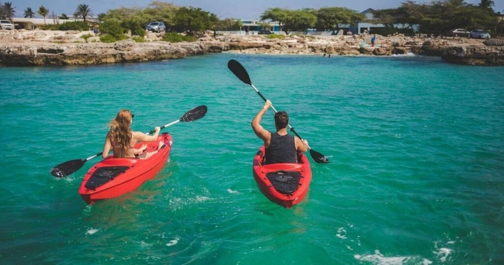Two people paddling red kayaks on turquoise water in Aruba