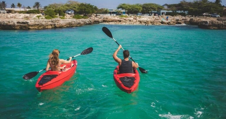 Two people paddling red kayaks on turquoise water in Aruba