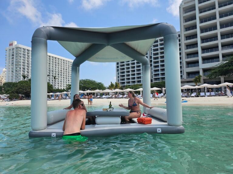 Guests chatting on a floating lounge deck in clear water with high-rise hotels behind